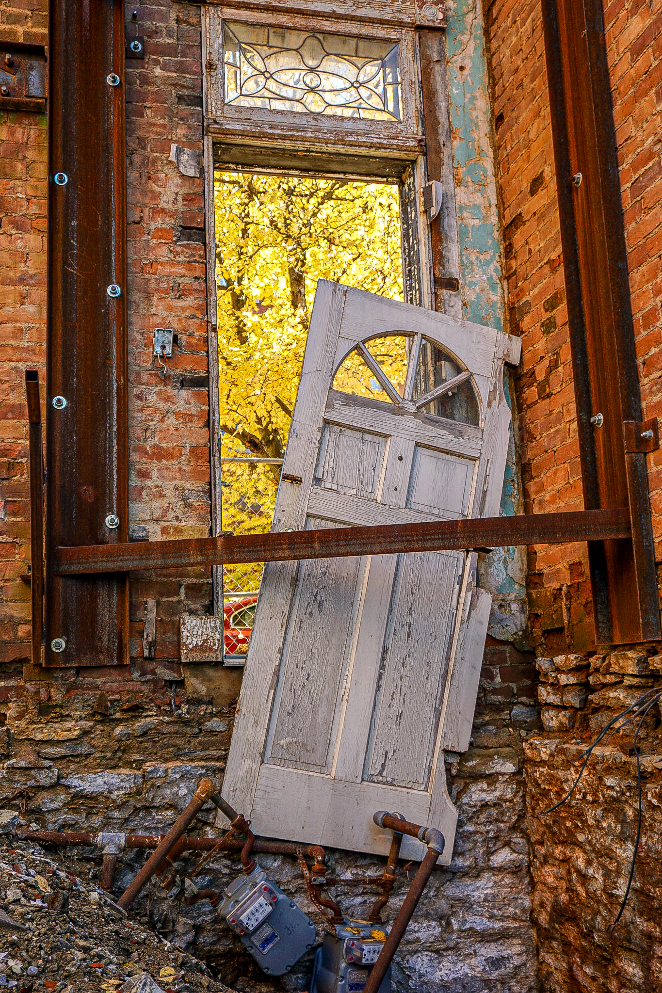 A collapsed painted door framing vivid autumn foliage through a crumbling brick wall.
