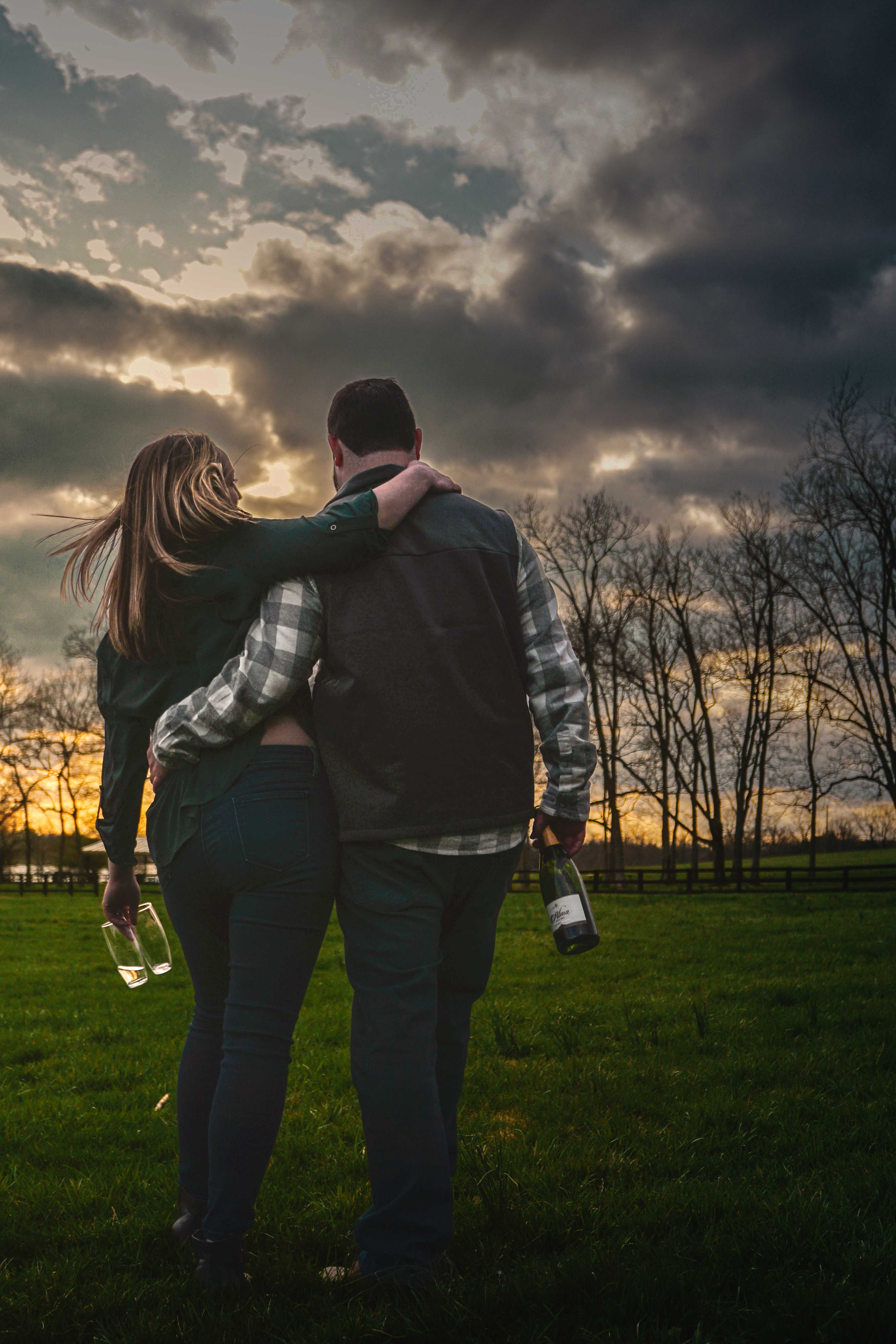Couple embracing at golden hour on a Kentucky farm, champagne in hand