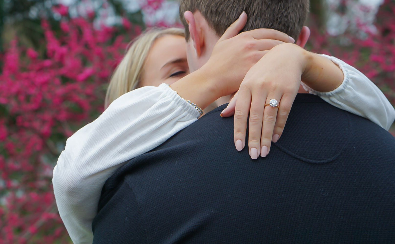 Engaged couple embracing in front of pink flowering trees